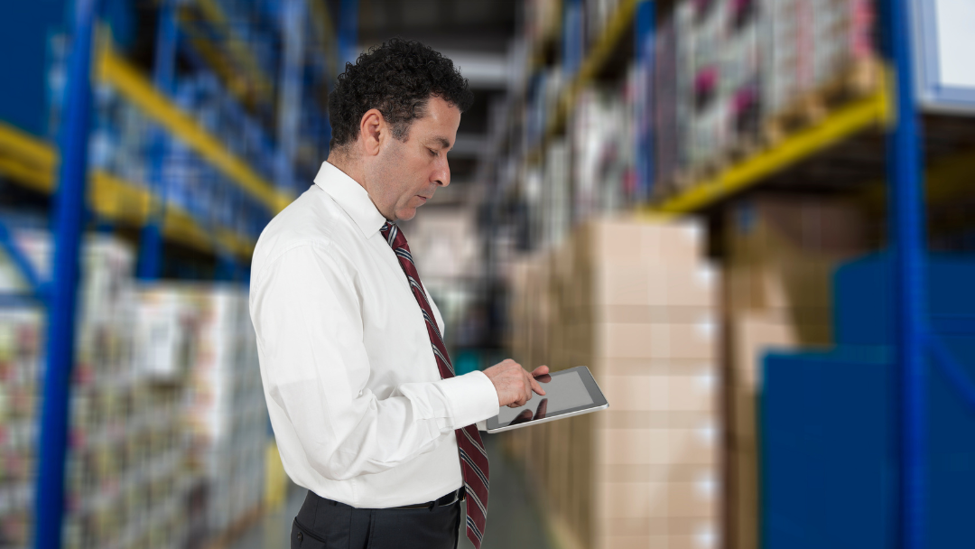 Factory manager checking inventory in stock room on touchscreen tablet